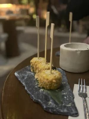 Aperitivos en brocheta sobre un plato oscuro con un tenedor y un bol al fondo.