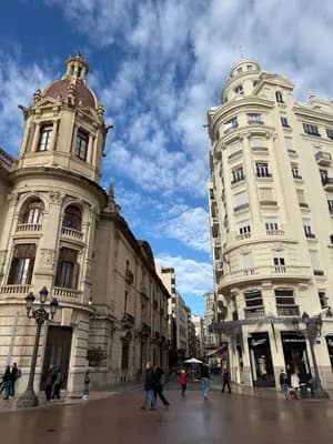 A street with ornate buildings and pedestrians under a partly cloudy sky.