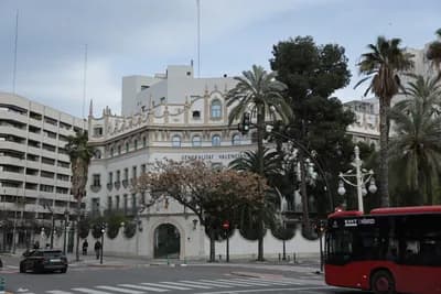 Historic building with palm trees and a red bus on a city street.