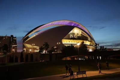 Modern curved building at dusk with people walking in the foreground.