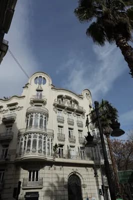 A historic building with intricate balconies and a palm tree against a clear sky.