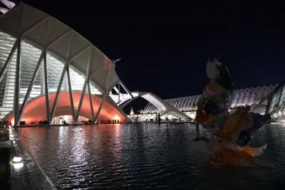 Modern architecture illuminated at night with a sculpture in the foreground.