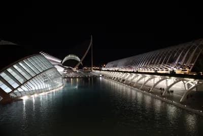 Modern architecture lit up at night, reflecting on water.