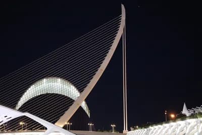 Modern architectural structure with crescent-shaped tower and cable design at night.