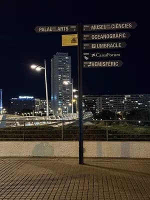 Nighttime directional signpost with illuminated signs pointing to Valencia landmarks.