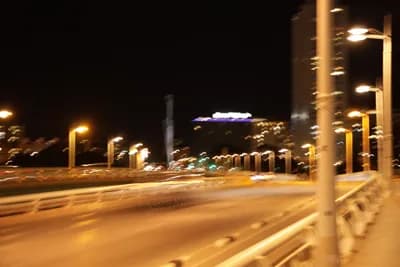 Blurred motion of vehicles on a bridge at night with illuminated streetlights and buildings.