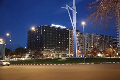 A modern hotel at night with illuminated signage and a tall sculpture.