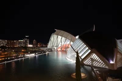 Modern architecture by a river at night with city lights in the background.