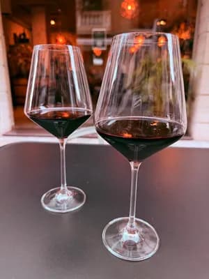 Two wine glasses filled with red wine on a dark table, softly lit background.