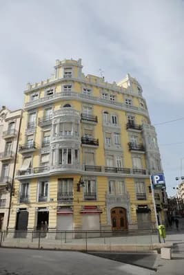 A yellow and gray ornate building with balconies and a parking sign in the foreground.