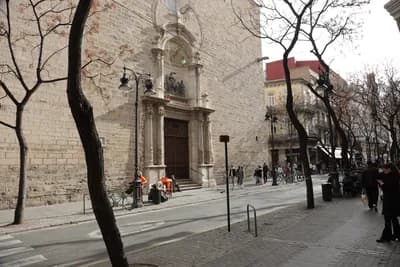 Historic stone building with large entrance, bare trees, pedestrians, sidewalk, street