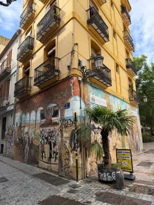 A colorful mural on a yellow building in a narrow street with cobblestone pavement.