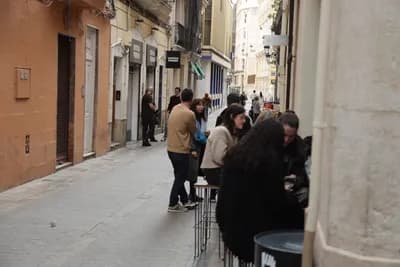 People sitting at an outdoor café in a narrow street with pastel-colored buildings.