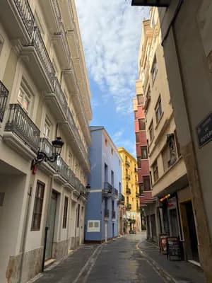 Narrow street with colorful buildings and a partly cloudy sky.