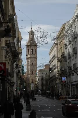 A street view in Valencia featuring a tall bell tower and holiday lights.