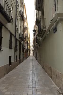 Narrow cobblestone street with tall buildings and balconies.