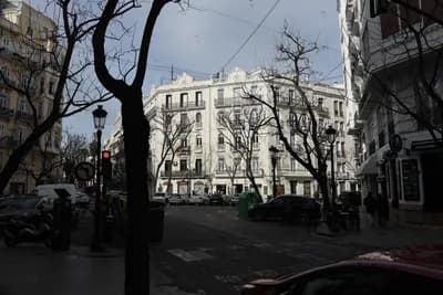 A street view with white buildings, bare trees, and parked cars under a clear sky.