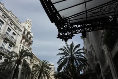 Ornate metalwork, palm trees, and classic architecture under a cloudy sky.