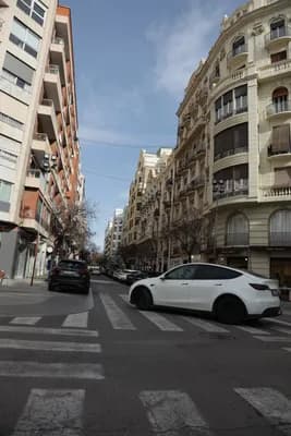 Quiet street with parked cars and residential buildings under clear sky.