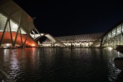 Modern architecture illuminated at night, reflecting on water.