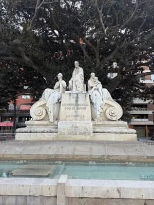 Statue of a man seated with two women and a child, surrounded by ornate architectural details and a fountain.
