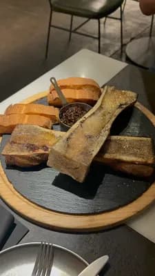 A plate of bone marrow with bread and sauce on a wooden and slate serving board.