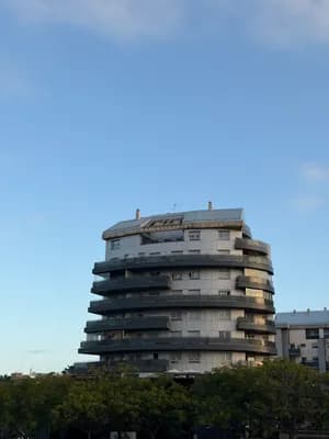 A modern building with curved balconies and a clear blue sky in the background.