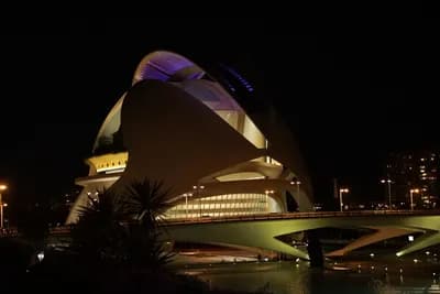 Modern illuminated architecture at night with a bridge in the foreground.