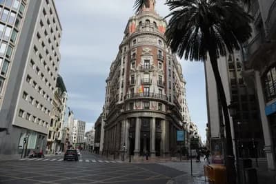 A grand, ornate building with a tower at the corner of a wide, empty street in Valencia, Spain.