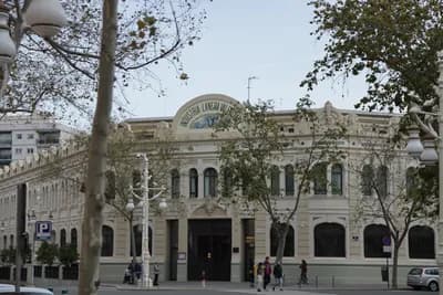 Historic building with ornate architecture and 'Industria Lámpara' sign, street scene with pedestrians and trees.