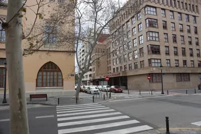 A street with a pedestrian crossing and parked cars in front of a multi-story building.
