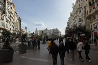 Pedestrians walking on a wide street with tall buildings and clear sky.