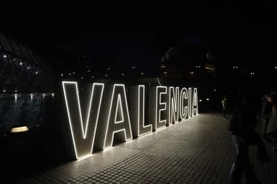 Illuminated 'VALENCIA' sign at night with people walking by.