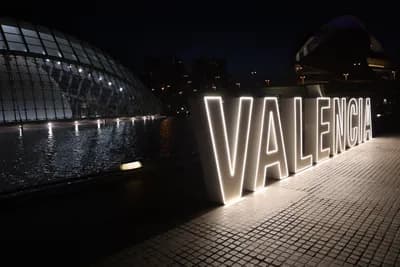 Illuminated 'VALENCIA' sign at night with modern architecture in the background.