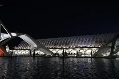 A futuristic building with curved white structures reflecting on water at night.