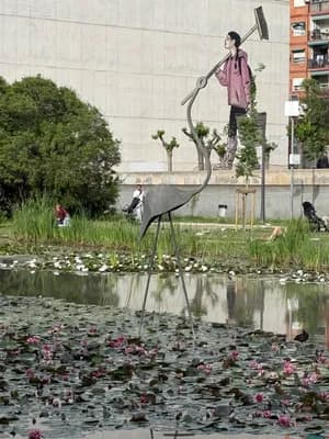 A sculpture of a bird and a person holding a rake in a pond with lily pads and greenery.
