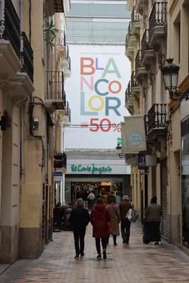 People walking in a narrow street with a large 'Blanco Color' advertisement and a 50% discount sign.