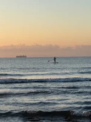 A silhouette of a paddleboarder on the ocean at sunset.