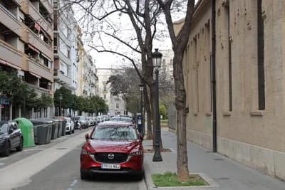 Red Mazda CX-5 parked on a quiet street with trees and buildings.