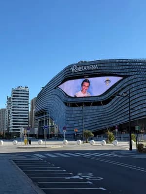 Modern stadium with a large digital screen and clear blue sky.