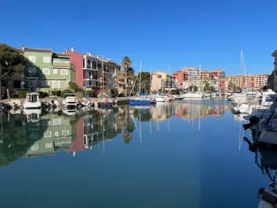 A serene marina with colorful buildings and boats reflected in still water.