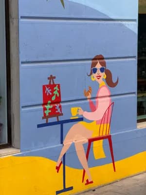 Colorful mural of a woman enjoying a cup and croissant next to an easel with a painting.
