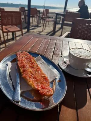 Tapas and coffee on a wooden table at a beachside cafe.