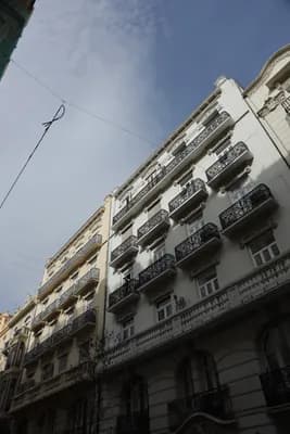 A multi-story building with decorative balconies and a partly cloudy sky above.