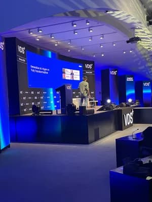 A person at a podium on a stage with a large screen displaying 'Generative AI: Hype vs Truly Transformative'.