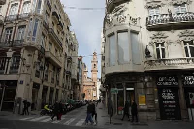 Pedestrians crossing a street in Valencia with historic architecture.