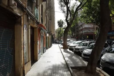A street scene with parked cars, trees, and closed storefronts.