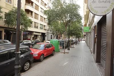 Urban street with parked cars, trees, and storefronts.