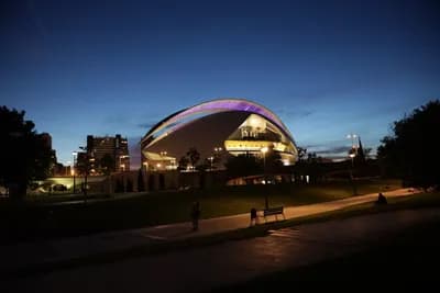 A modern, illuminated building with a curved roof at dusk.