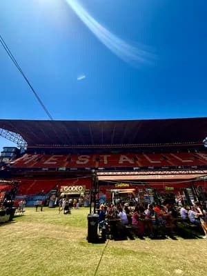 People enjoying a sunny day at a stadium with a canopy and grassy area.